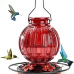 A vibrant red glass hummingbird feeder by Grete Gotye, hanging outdoors with five metal flower feeding ports.