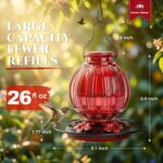 A vibrant red glass hummingbird feeder by Grete Gotye, hanging outdoors with five metal flower feeding ports.