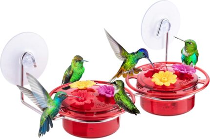 A vibrant red iBorn window hummingbird feeder with clear nectar reservoir, attached to a window pane via a large suction cup,