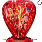 A vibrant hand-blown glass hummingbird feeder with a floral balloon design, hanging outdoors in a garden.