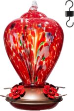 A vibrant hand-blown glass hummingbird feeder with a floral balloon design, hanging outdoors in a garden.