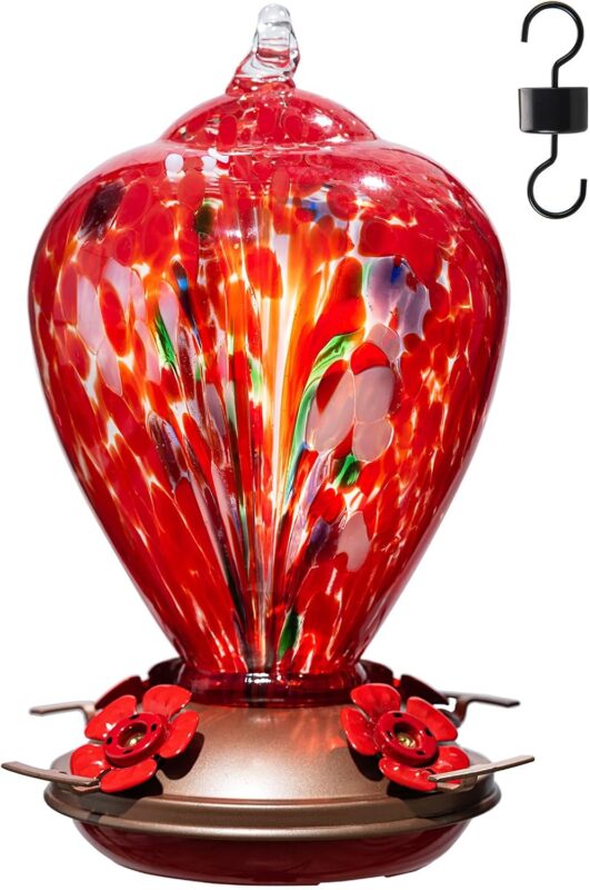 A vibrant hand-blown glass hummingbird feeder with a floral balloon design, hanging outdoors in a garden.