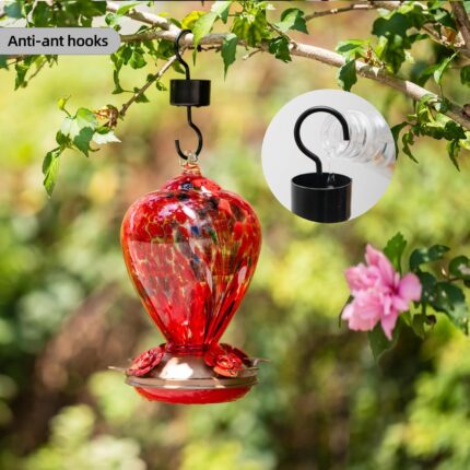 A vibrant hand-blown glass hummingbird feeder with a floral balloon design, hanging outdoors in a garden.