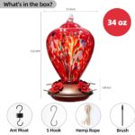 A vibrant hand-blown glass hummingbird feeder with a floral balloon design, hanging outdoors in a garden.