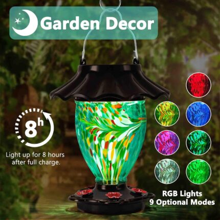 A teal hand-blown glass LUJII solar-powered hummingbird feeder hanging outdoors, glowing with color-changing light at dusk.