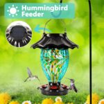 A teal hand-blown glass LUJII solar-powered hummingbird feeder hanging outdoors, glowing with color-changing light at dusk.
