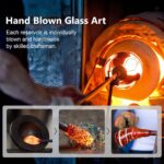 A teal hand-blown glass LUJII solar-powered hummingbird feeder hanging outdoors, glowing with color-changing light at dusk.