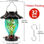 A teal hand-blown glass LUJII solar-powered hummingbird feeder hanging outdoors, glowing with color-changing light at dusk.